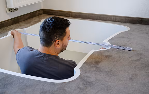 Ein Mann misst mit einem Zollstock die Breite des Deckenausschnitts ab und nimmt somit die Bauabnahme für den weiteren Einbau des Lifton Homelifts ab.