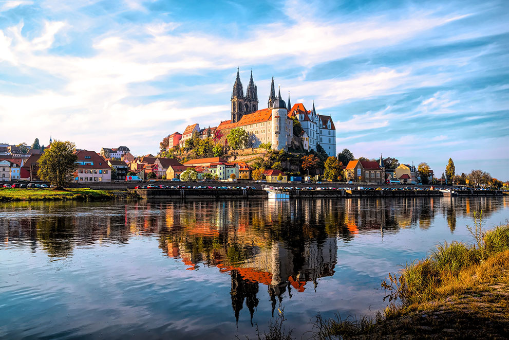 Das Bild zeigt die Stadt Magdeburg; der Magdeburger Dom dominiert das Stadtbild, steht ruhig im Zentrum, die Elbe fließt im Vordergrund, moderne und historische Gebäude sind sichtbar
