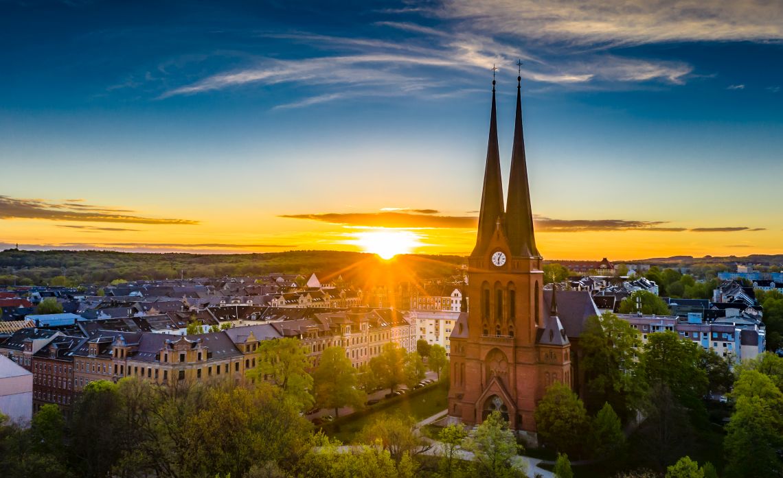 Blick auf eine Kirchenspitze und die Dächer der Stadt Chemnitz bei Sonnenuntergang
