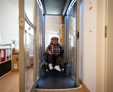Kleinwüchsiger Mann sitz im Rollstuhl im Homelift