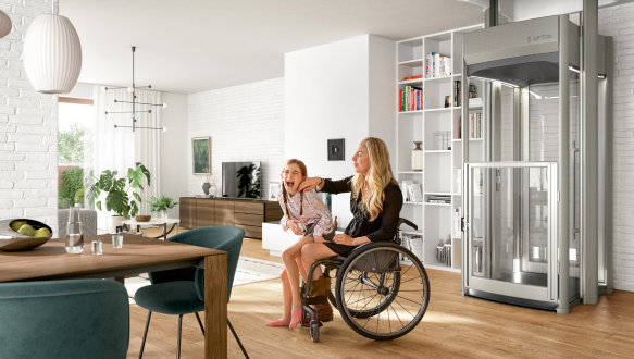 Zwei Personen sitzen lachend im Wohnzimmer, eine im Rollstuhl, neben ihnen steht ein moderner Homelift von Lifton in einer offenen, hellen Wohnumgebung.