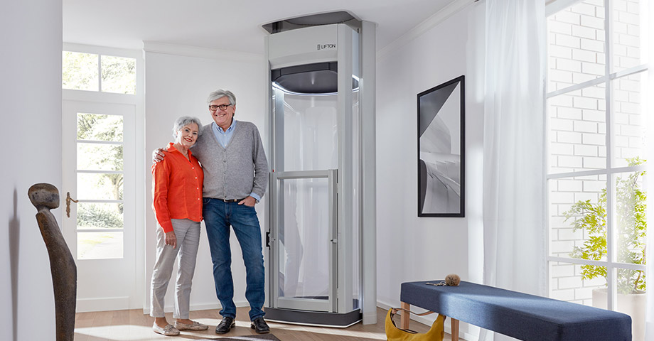 Infopaket: kostenlos anfordern Seniorenpaar steht Arm in Arm neben einem Homelift